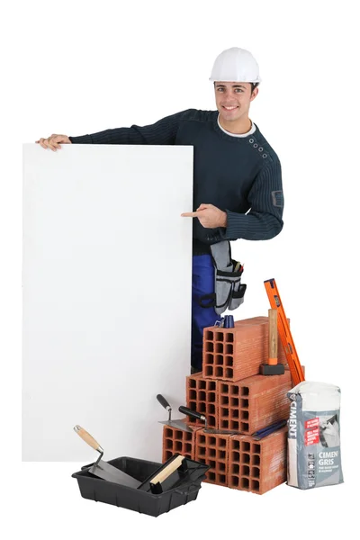Pedreiro posando com seus materiais de construção e um sinal em branco — Fotografia de Stock