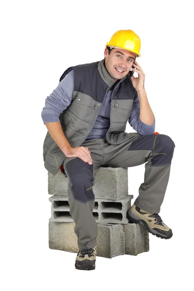 Mason speaking on the telephone whilst sat on breeze block — Stock Photo, Image