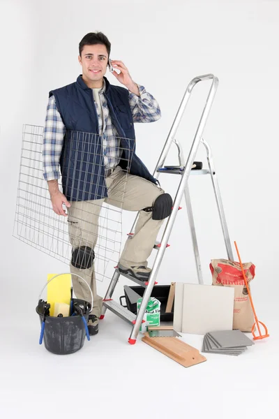 Handwerker posiert mit seinen Baumaterialien und telefoniert mit seinem Handy — Stockfoto