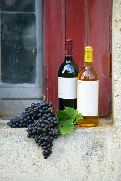 Garrafas de vinho e cachos de uvas em um parapeito da janela — Fotografia de Stock