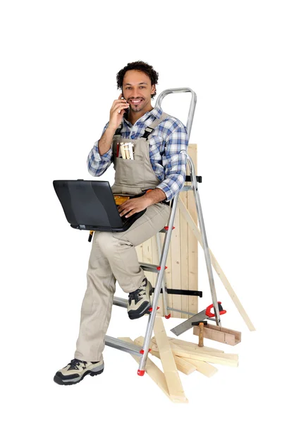 Carpinteiro empoleirado na escada enquanto faz uma chamada telefónica — Fotografia de Stock