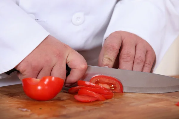 Um cozinheiro cortando um tomate — Fotografia de Stock