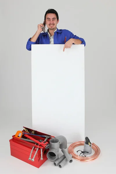 Tradesman with a cellphone and a board left blank for your message — Stock Photo, Image