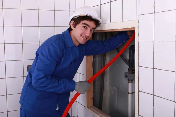 Electricista alimentando tubería roja detrás de una pared de azulejos — Foto de Stock
