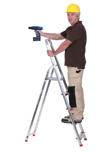 Comerciante usando una herramienta eléctrica mientras está de pie sobre una escalera —  Fotos de Stock