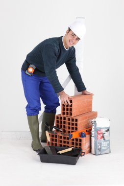 A bricklayer posing with his tools and building materials clipart