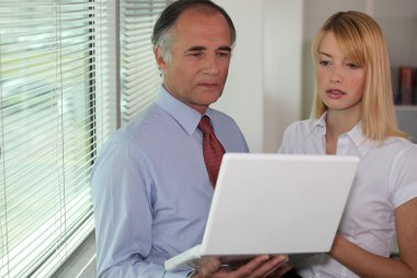 Businessman looking at a laptop with his assistant clipart