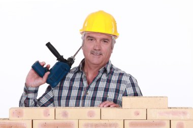 Tradesman holding a power tool and standing behind a brick wall clipart