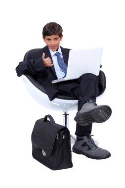 Boy dressed in a businessman using a laptop computer making a 'telephone' sign with his hand clipart