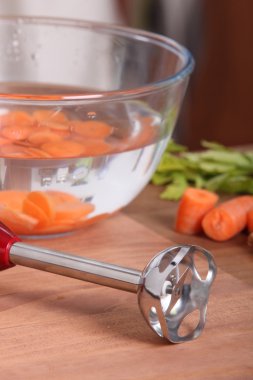 Hand blender and sliced carrots in water clipart