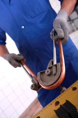 Worker using a tool to bend a copper tube clipart