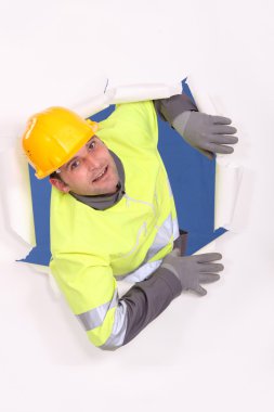 A male construction worker who went through a wall of paper. clipart