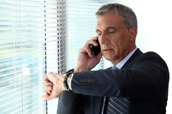 Businessman checking time whist on telephone call — Stock Photo, Image