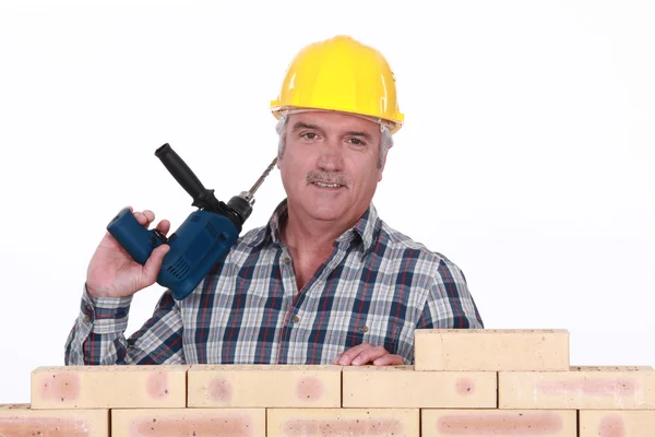 Handelaar holding een machtshulpmiddel en permanent achter een bakstenen muur — Stockfoto