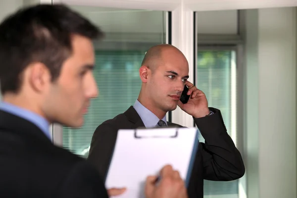 Un homme d'affaires tenant une pince pendant qu'un collègue fait un appel téléphonique — Photo