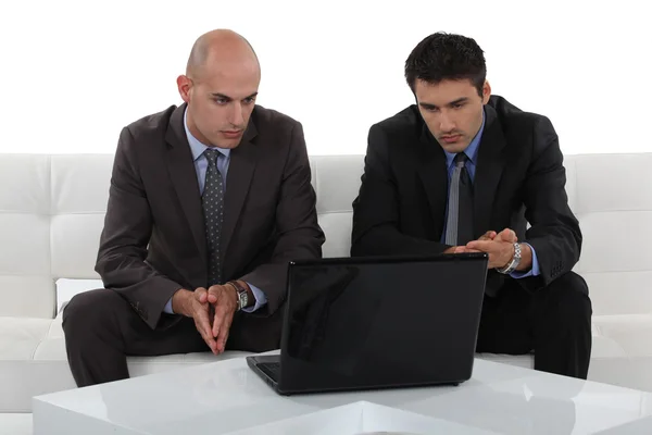Due uomini d'affari seduti su un divano a guardare qualcosa su un computer portatile — Foto Stock