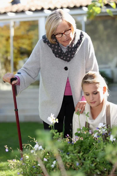 Mujer mayor en un jardín con una joven ayudante — Foto de Stock