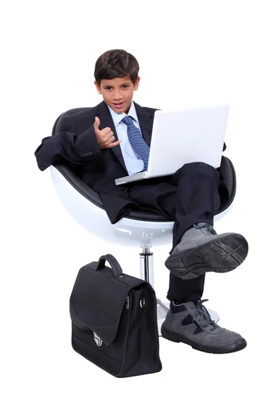Niño vestido con un hombre de negocios usando una computadora portátil haciendo un cartel de 'teléfono' con su mano —  Fotos de Stock
