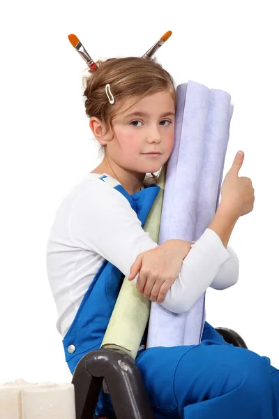 Little girl wearing painter's overalls and holding wallpapers — Stock Photo, Image