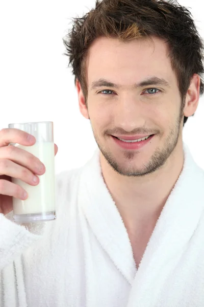 Young man wearing a bathrobe and drinking a glass of milk — Stock Photo, Image