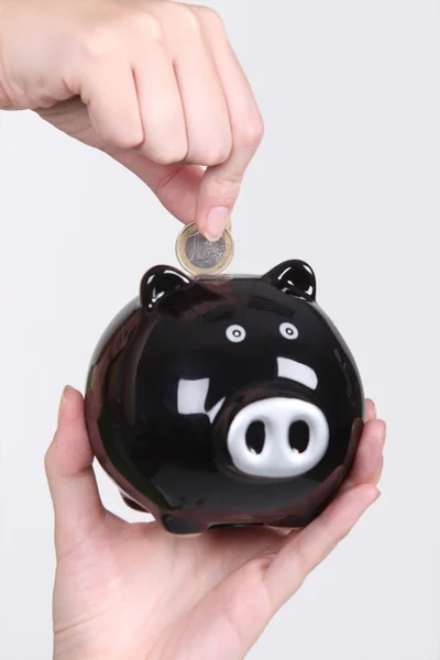 Hand een euromunt invoegen in een zwarte piggy bank — Stockfoto