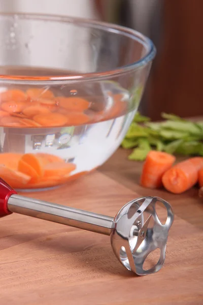 Ручной блендер и нарезанная морковь в воде — стоковое фото
