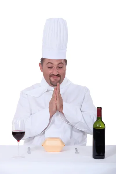 Шеф-повар сидит между бокалом вина и бутылкой вина и стоящим перед гамбургером — стоковое фото