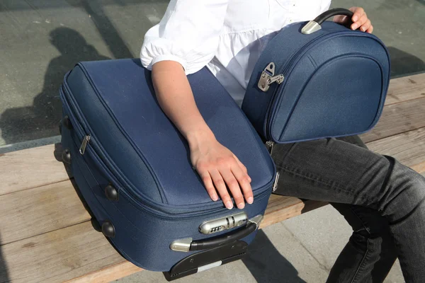 Женщина сидит на скамейке с чемоданом — стоковое фото