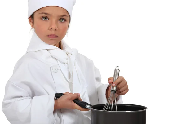 A little girl dressed in chief cook uniform is cooking — Stock Photo, Image