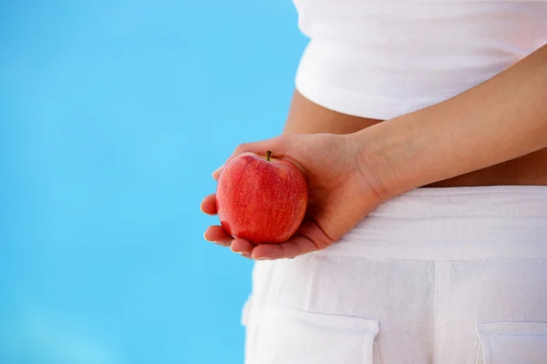 Kobieta trzyma jabłko za jej plecami — Zdjęcie stockowe