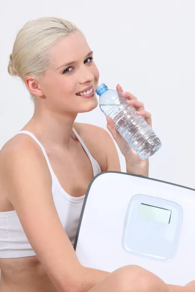 Jovem de roupa interior branca bebendo água engarrafada e segurando balanças eletrônicas — Fotografia de Stock