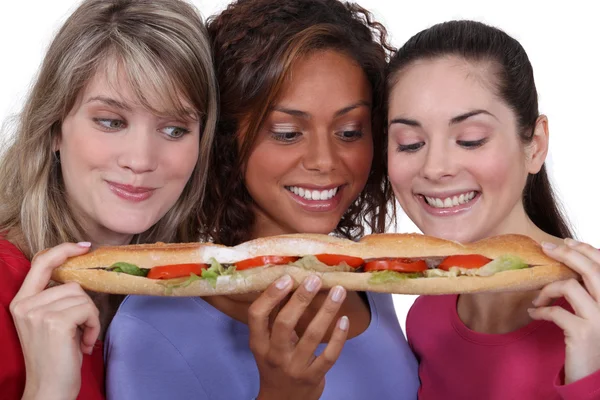 Three female friends sharing long sandwich — Stock Photo, Image
