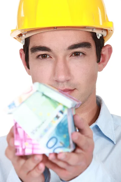 Builder with a house made of money — Stock Photo, Image
