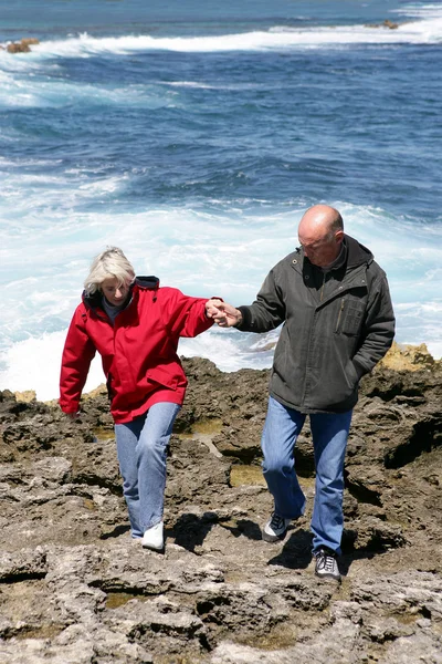 Casal maduro andando ao longo de uma costa rochosa — Fotografia de Stock