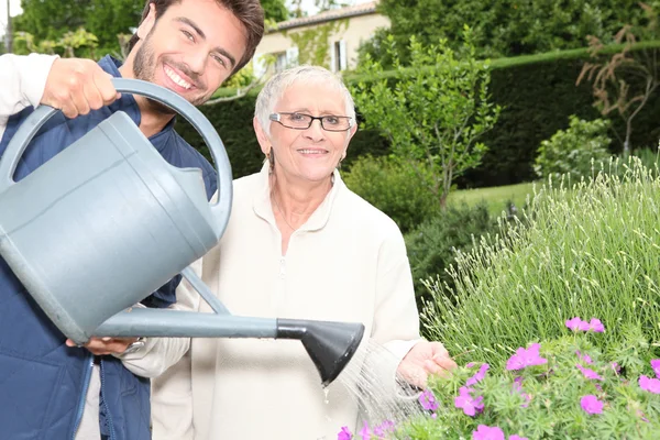 Young man watering plants with older woman — Stock Photo, Image