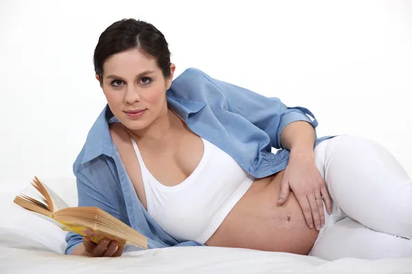 Mujer embarazada acariciando su vientre embarazada mientras lee —  Fotos de Stock
