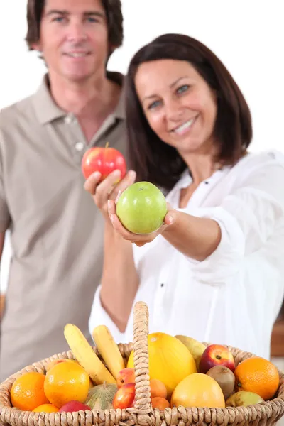 Mujer parada frente a la cesta de frutas sosteniendo manzanas — Foto de Stock