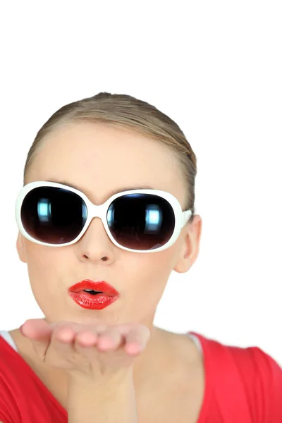 Женщина в солнечных очках, дующая в поцелуи на белом фоне — стоковое фото