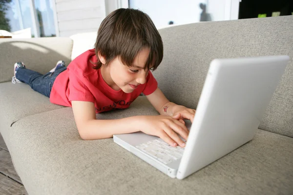 Menino usando um laptop no sofá — Fotografia de Stock