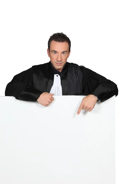Man in black robes pointing at a board left blank for message — Stock Photo, Image