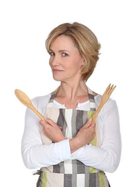 Woman wearing apron with wooden salad servers and an odd expression — Stockfoto