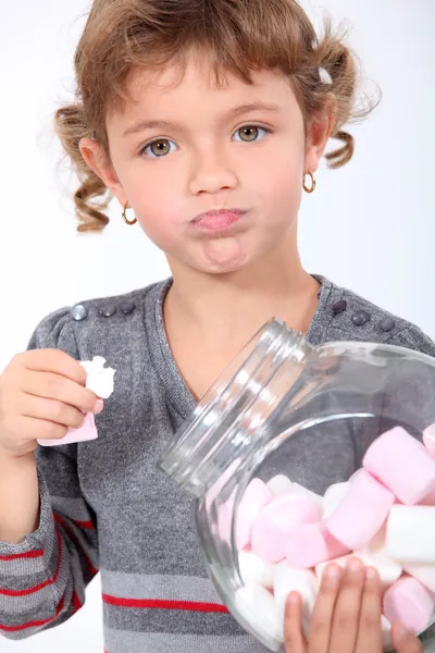 Little girl eating marshmallows from a jar — Stock Photo, Image