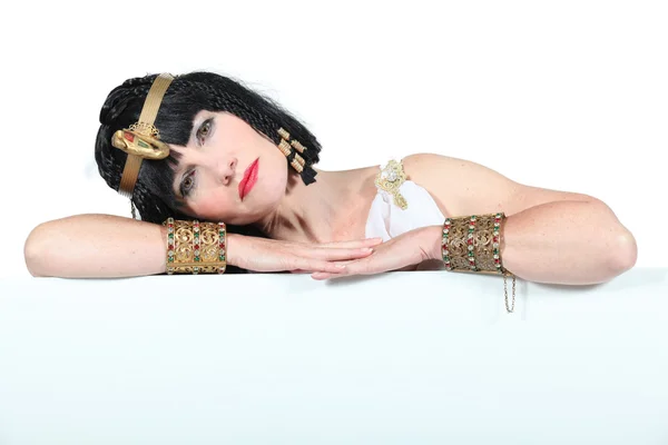 Als Kleopatra verkleidete Frau lehnt sich an ein Brett, das für Bild oder Text leer gelassen wird — Stockfoto