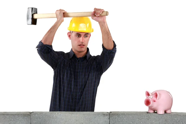一名建筑工人，用铁锤打开储钱罐. — 图库照片
