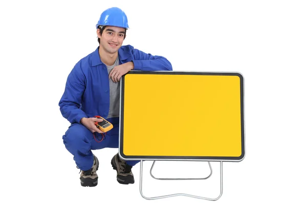 An electrician kneeled next to a blank road sign. — Stockfoto
