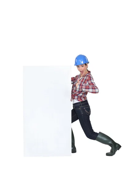 Een vrouwelijke bouwvakker door een billboard. — Stockfoto