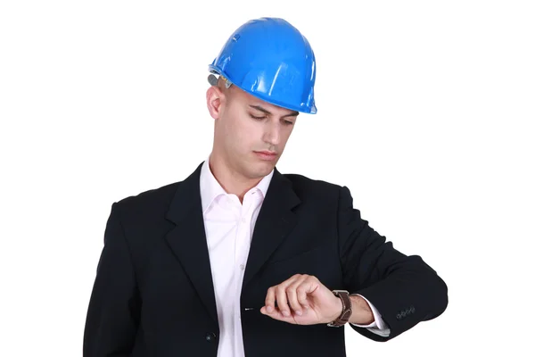 Мужчина в каске в костюме смотрит на часы — стоковое фото