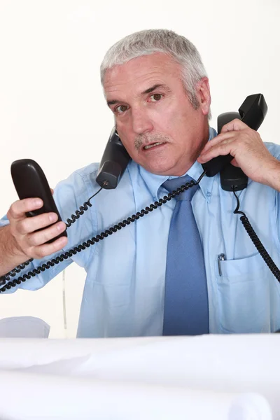Overwhelmed man answering ringing telephones — Stock Photo, Image