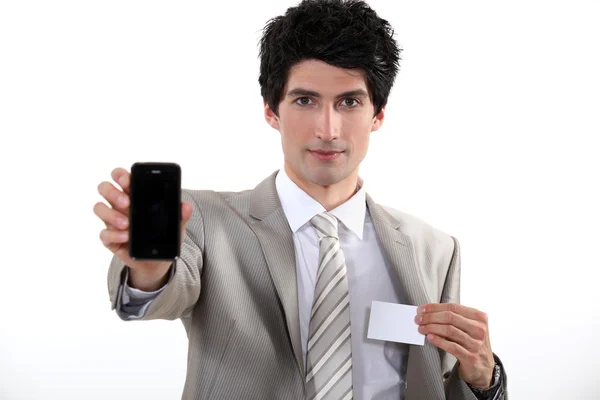 Businessman holding a blank business card and his phone — Stock Photo, Image
