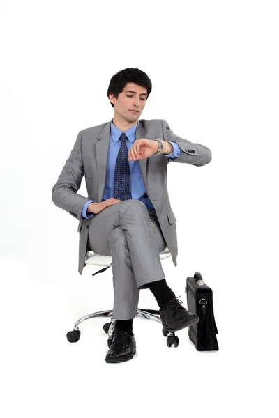 Сідаючий бізнесмен дивиться на свій годинник — стокове фото
